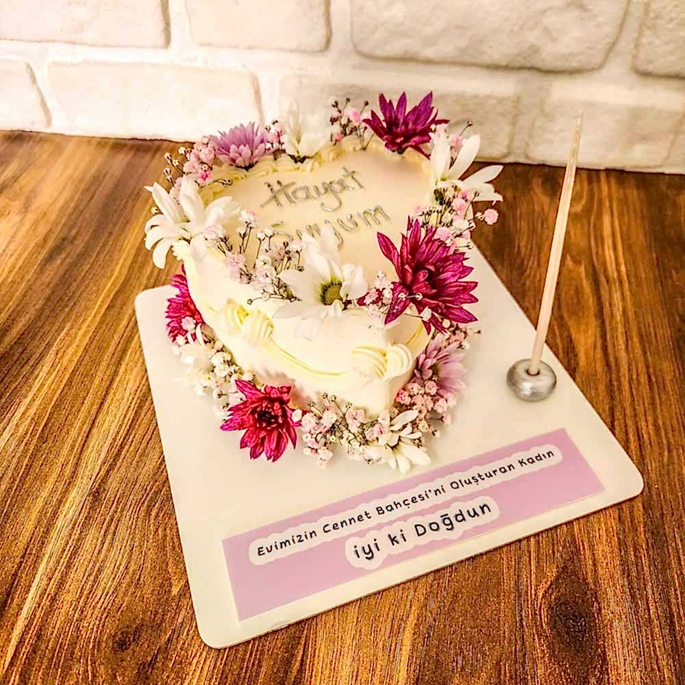 Kalp formunda tasarlanmış butik pasta, canlı çiçeklerle süslenmiş; romantik ve doğal bir atmosfer sunan özel kutlama pastası.