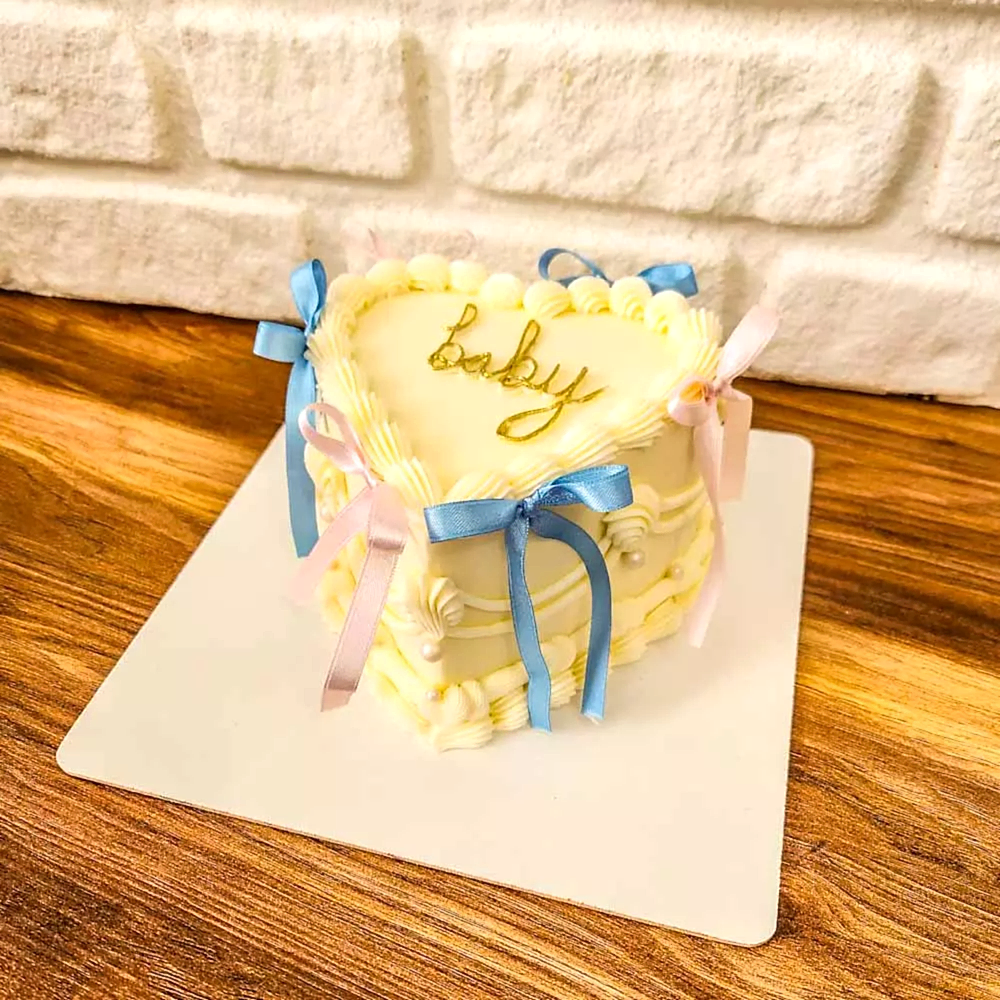 Beyaz zeminli butik pasta, üzerinde “Kız mı? Erkek mi?” yazısı ve pembe-mavi detaylarla süslenmiş; cinsiyet partileri için eğlenceli ve merak uyandıran bir tasarım.