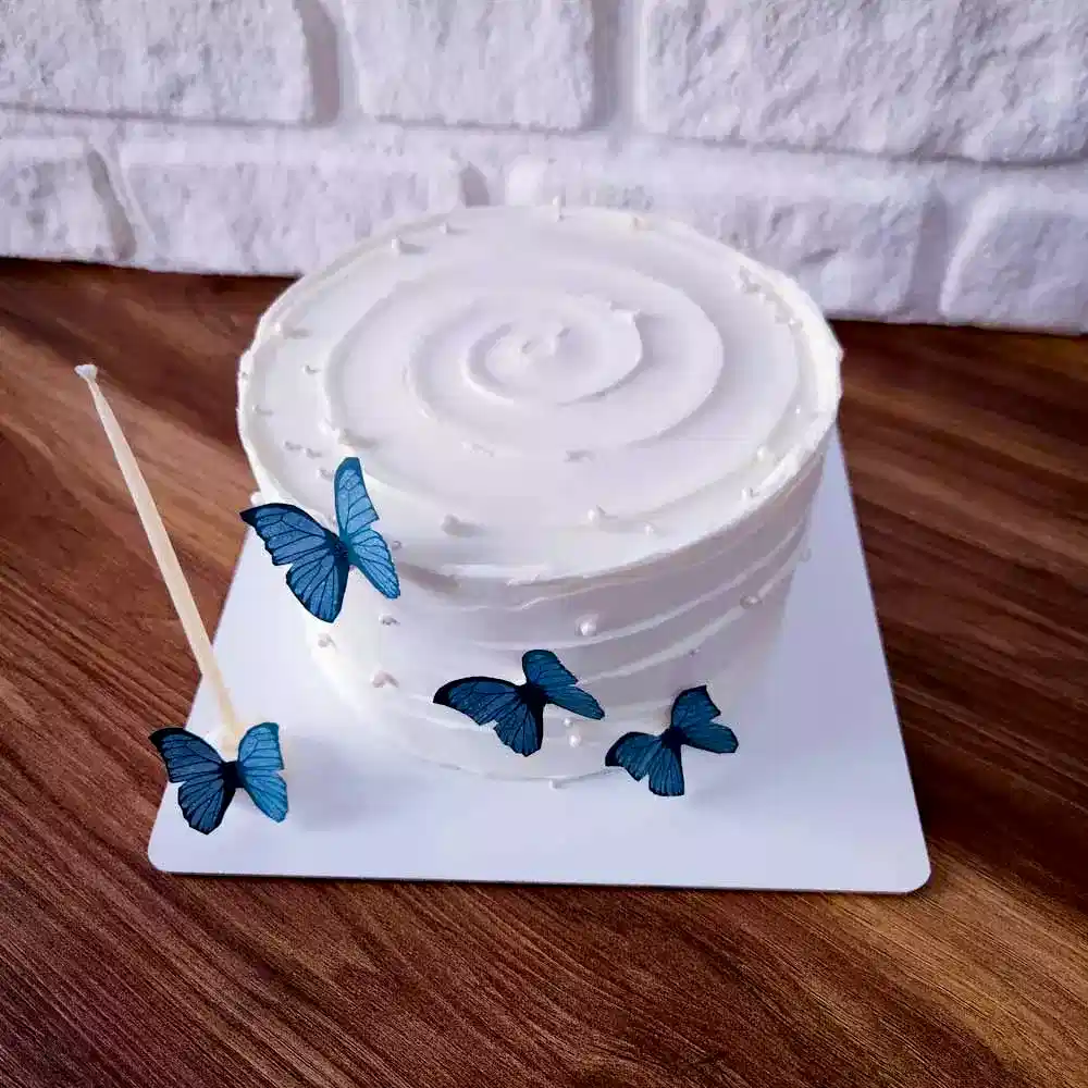 Küçük boyutlu, sade ve şık tasarıma sahip bento pasta; üstü kremadan yapılmış zarif kelebek figürleriyle süslenmiş. Hem romantik hem pastel tonlarda sunulan bu tasarım, özel günlere zarafet katıyor.