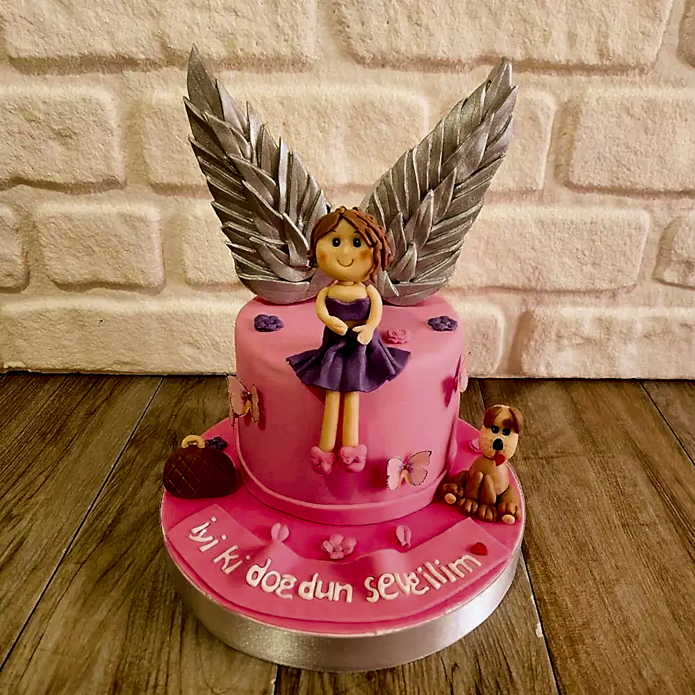 Küçük kız, çanta ve melek kanatlı köpek figürleriyle süslenmiş duygusal butik pasta. Sevgi dolu bir anıya özel tasarım.