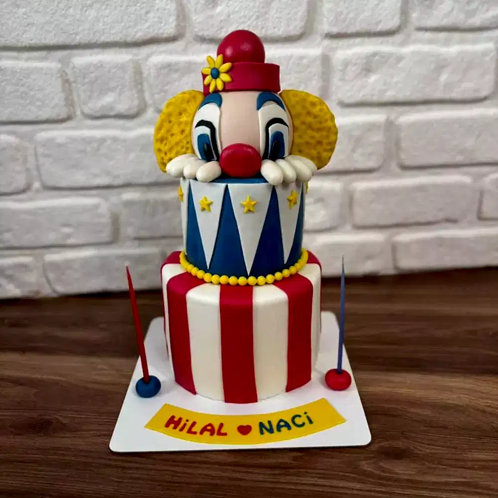 İki katlı yapısı ve en üstteki palyaço kafası figürüyle süslenmiş eğlenceli butik pasta. Renkli kutlamalara özel tasarım.