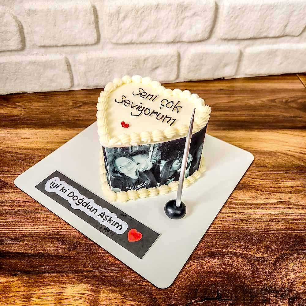 Kalp formunda tasarlanmış butik pasta, dış kaplaması minik fotoğraflarla süslenmiş; üzerinde yazılı mesajıyla hem görsel hem duygusal bir kutlama sunar.